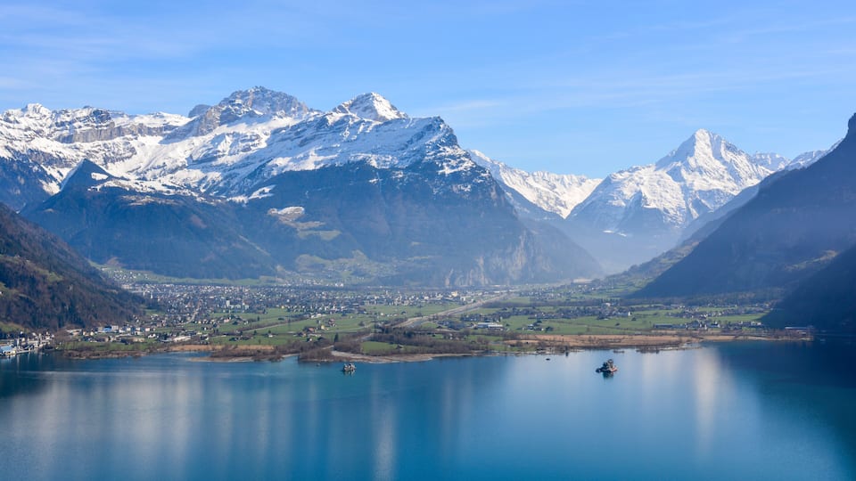 A lake surrounded by snow-capped mountains and a small town in the valley.