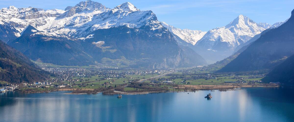 A lake surrounded by snow-capped mountains and a small town in the valley.