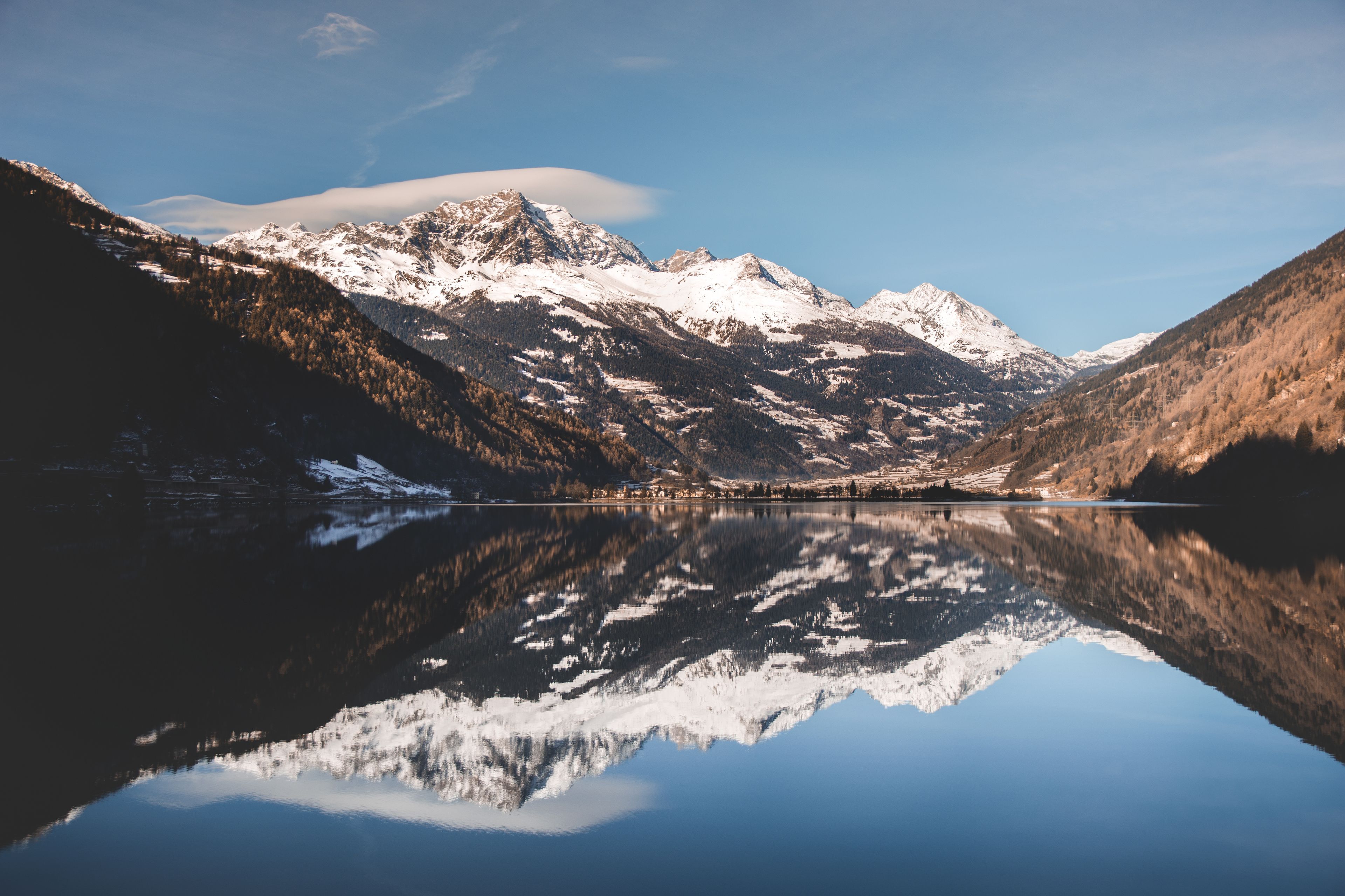 Cordillera nevada, un lago transparente que refleja las montañas y un valle cubierto de bosque.
