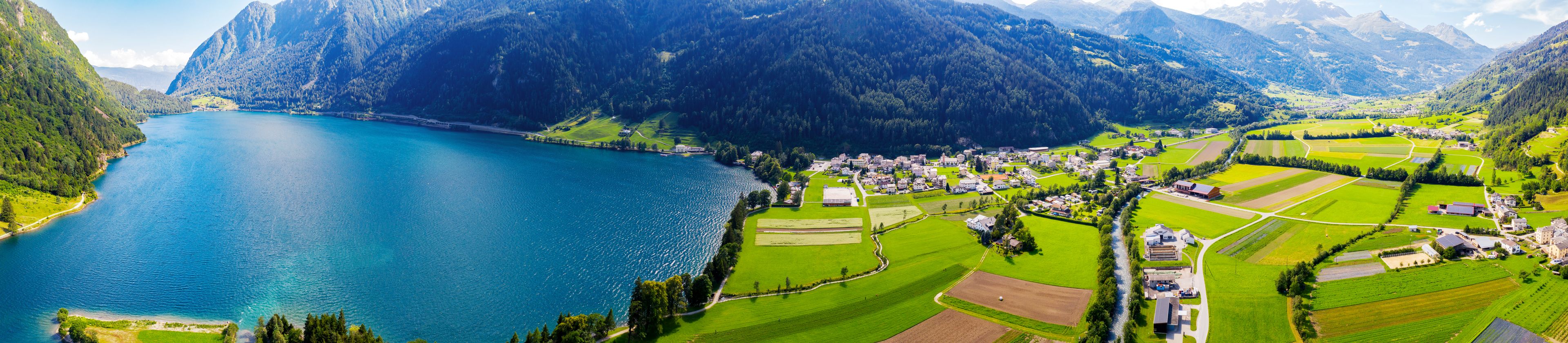 Un lago rodeado de montañas, un pueblo con campos verdes y un cielo despejado.