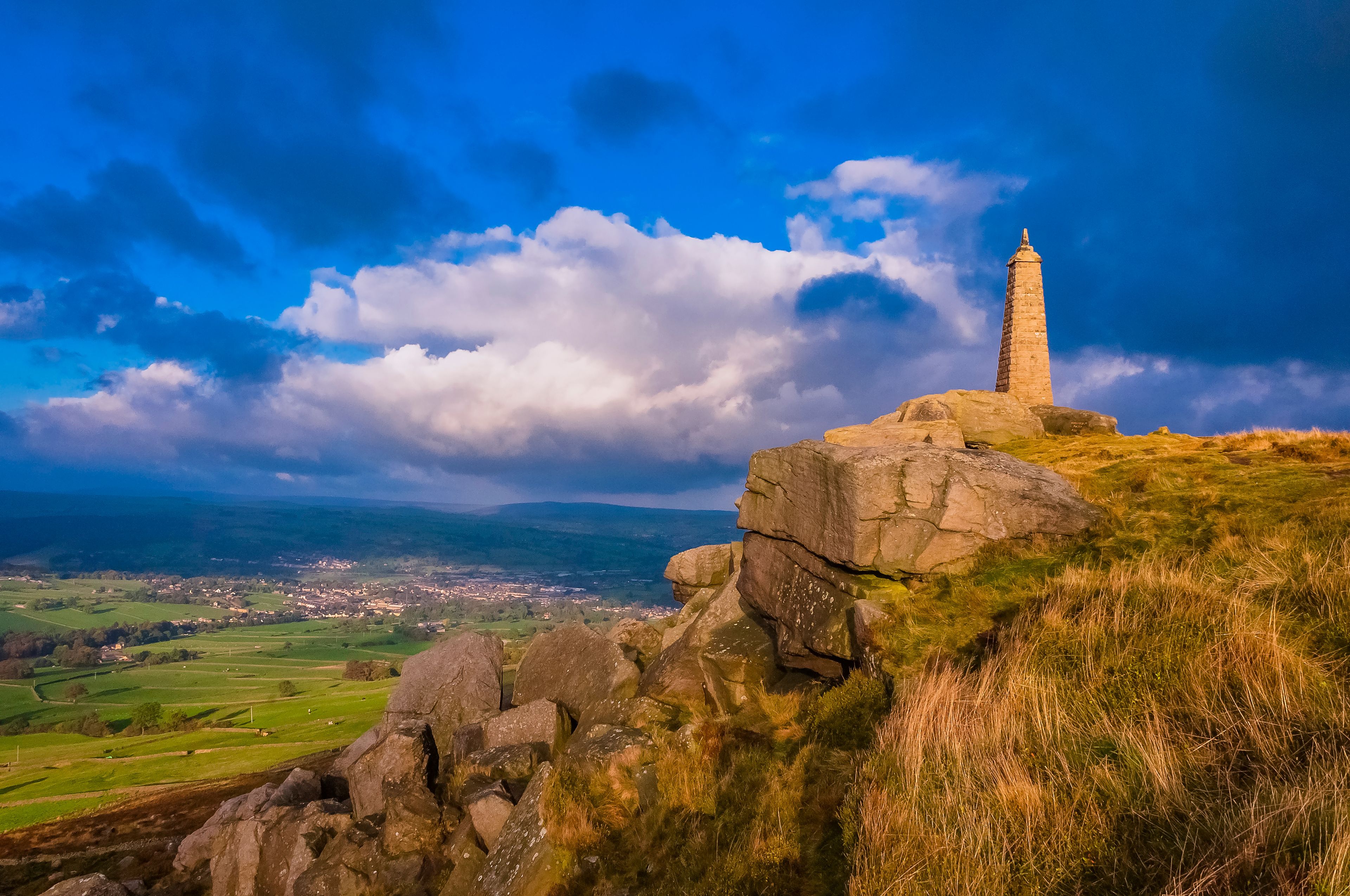 A stone monument on a hilltop with a view of a valley and a town below.