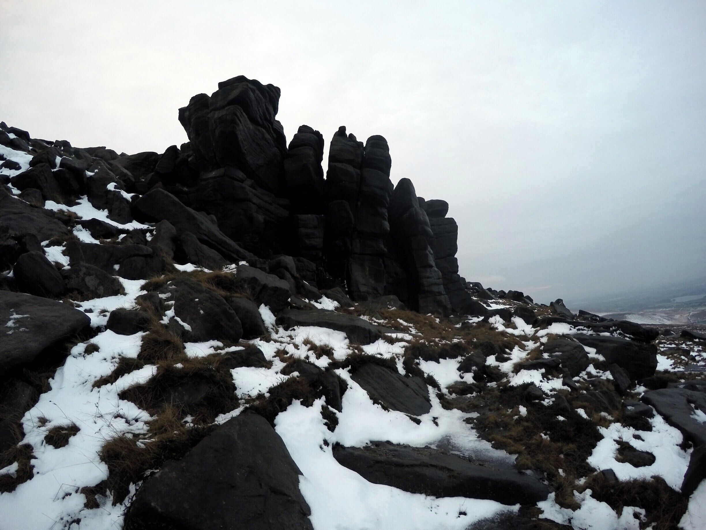 A rocky mountain landscape with snow patches and a distant view of a valley.