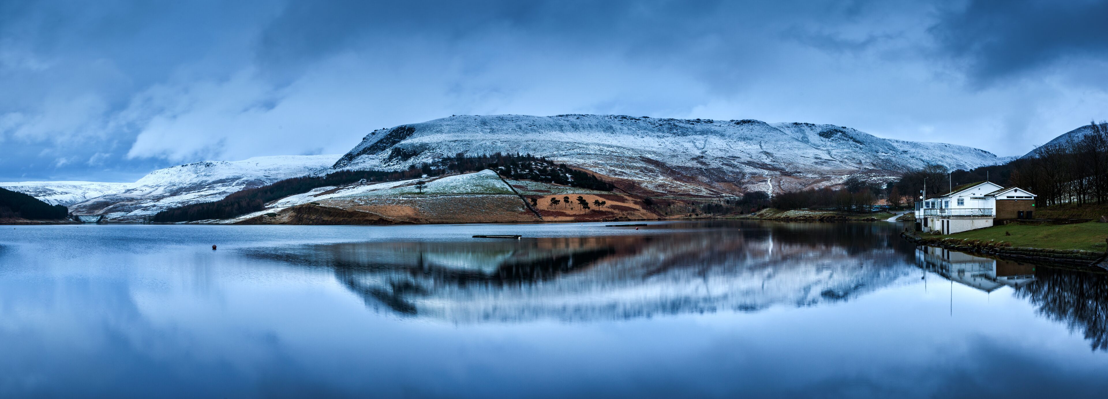 A snow-covered mountain, a calm lake, and a small building near the shore.