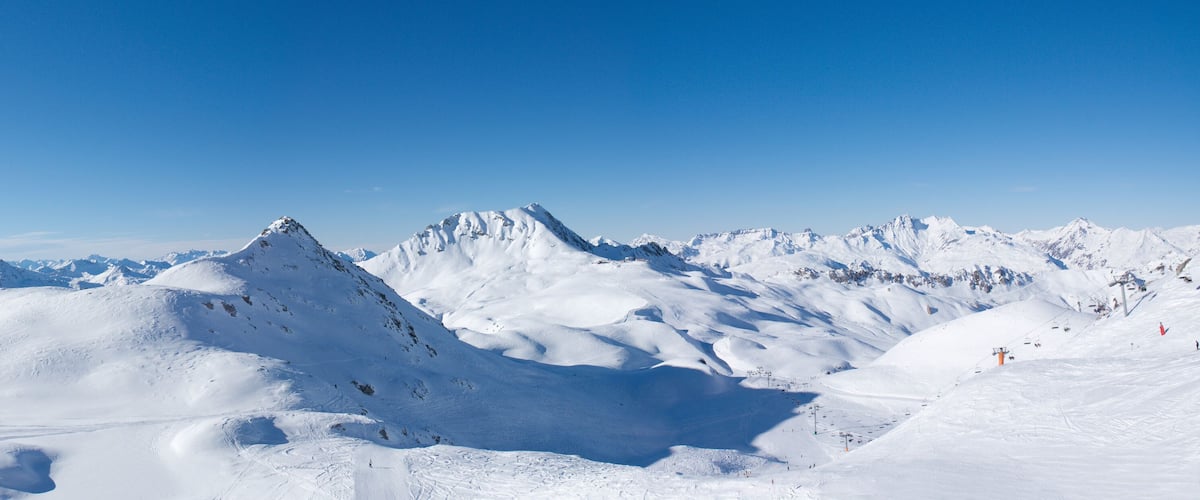A snow-covered mountain range with ski slopes and a clear blue sky.