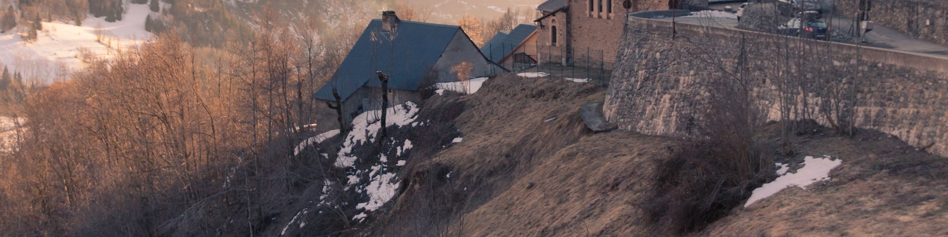 A mountain village with a church, stone buildings, and snow-covered peaks.