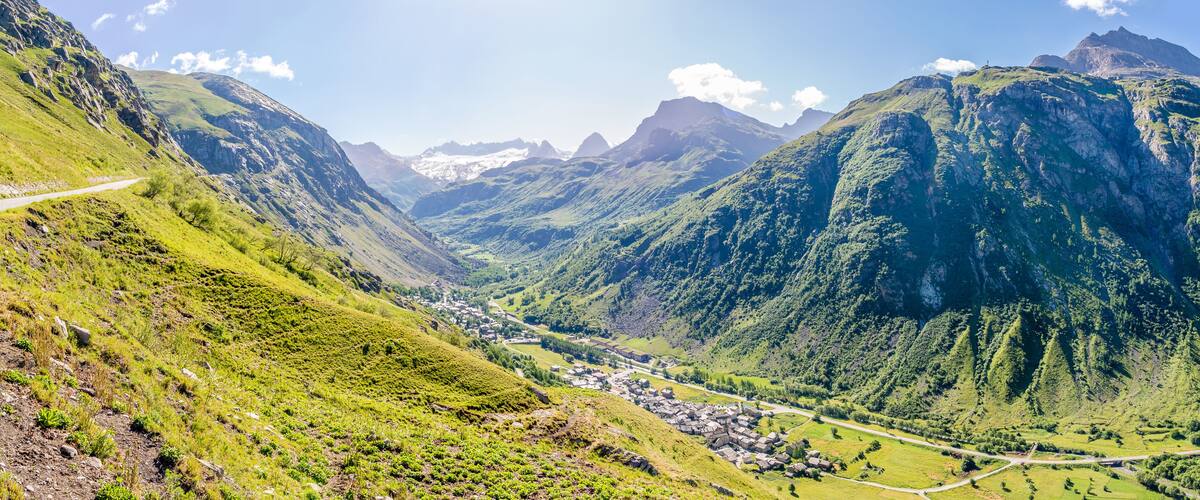 Un valle con una carretera serpenteante, colinas verdes y un pequeño pueblo.