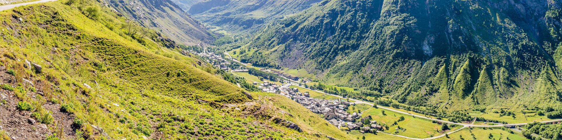 A valley with a winding road, green hills, and a small village.