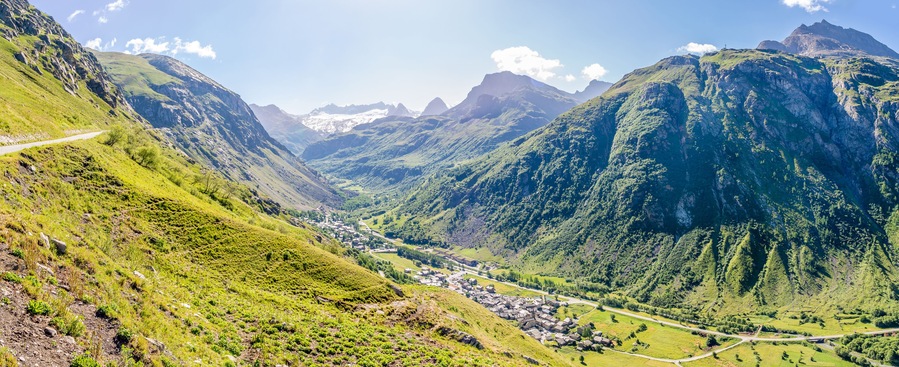 Un valle con una carretera serpenteante, colinas verdes y un pequeño pueblo.