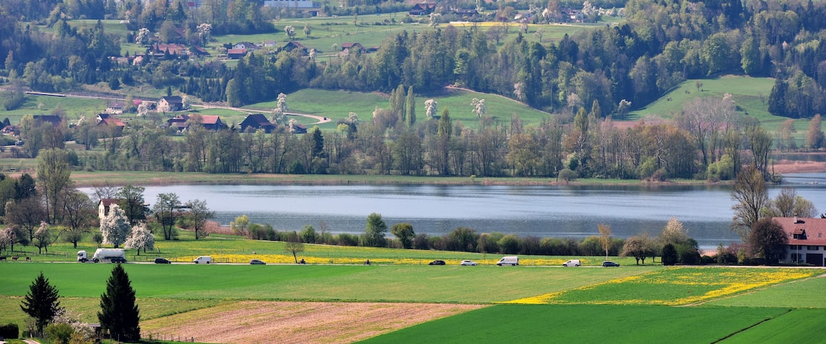A lakeside town with green fields, a church, and a river.