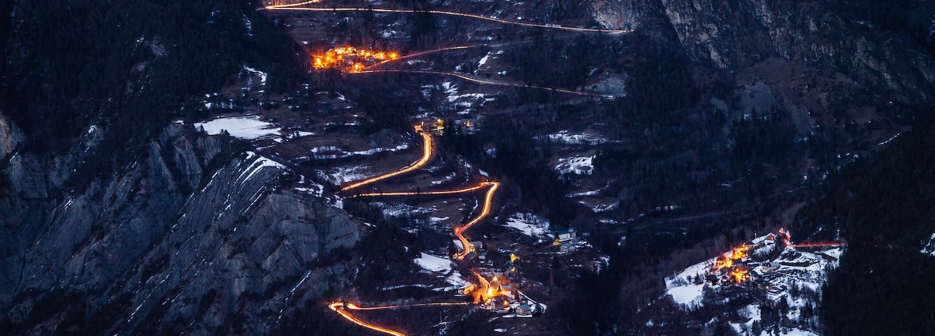 Un paisaje montañoso cubierto de nieve, con carreteras sinuosas y edificios iluminados.