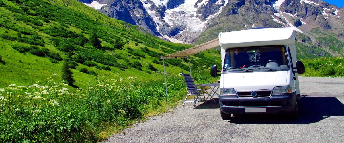 A white camper van parked on a road with a mountainous backdrop.