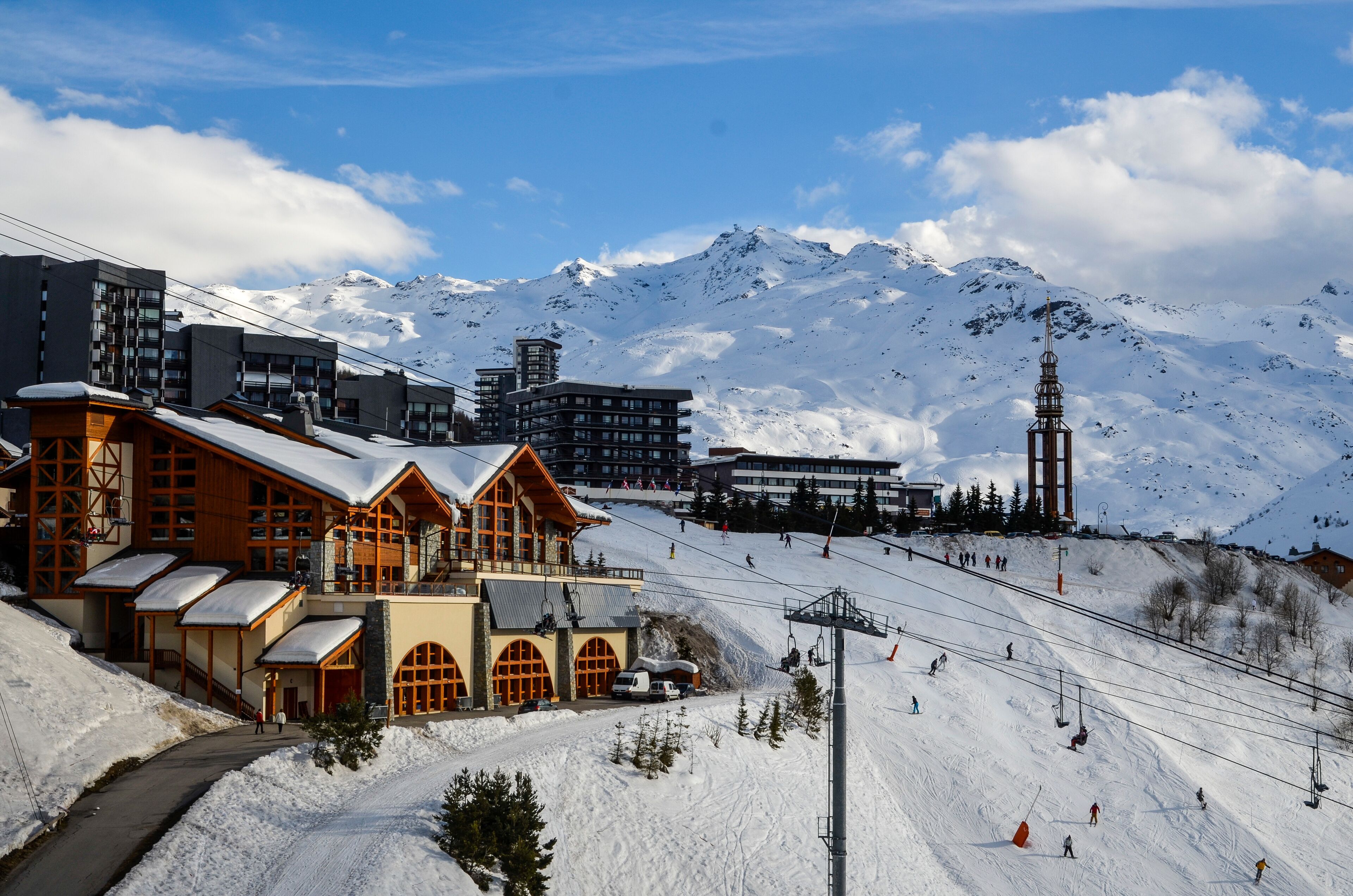 A ski resort with wooden buildings, a ski lift, and a snow-covered mountain in the background.