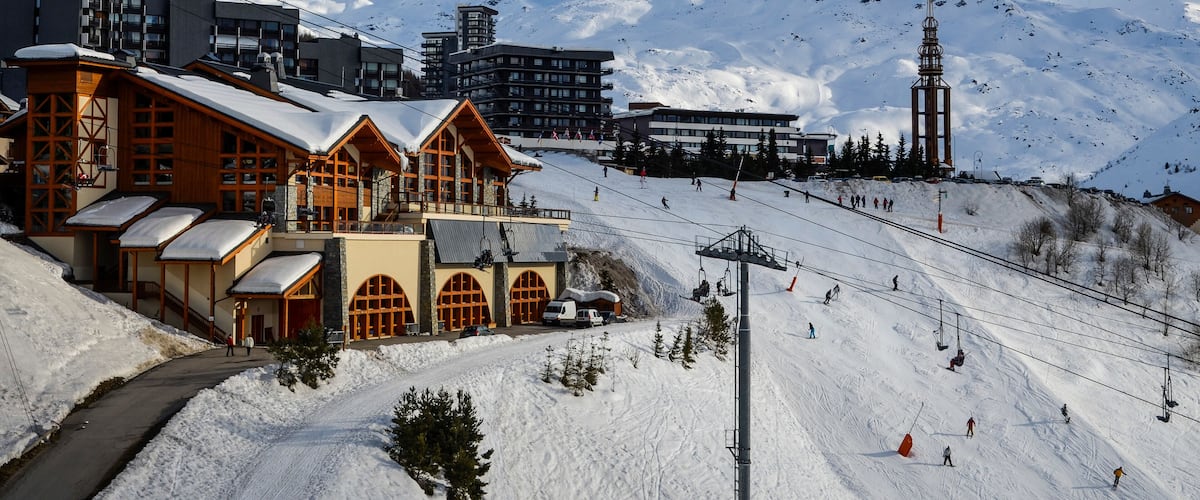A ski resort with wooden buildings, a ski lift, and a snow-covered mountain in the background.
