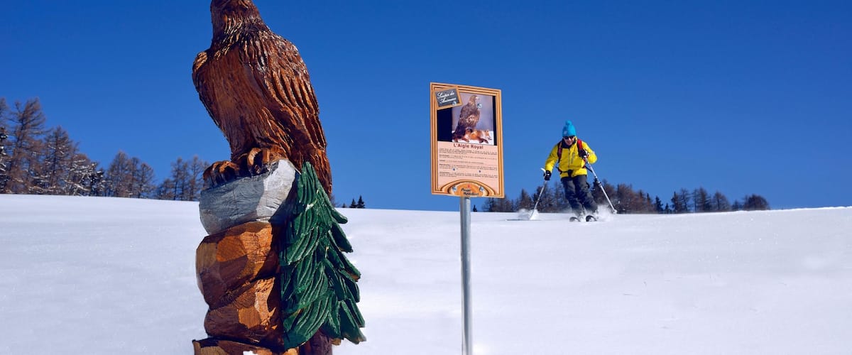 A wooden sculpture of an eagle, a sign, and a skier in the background.
