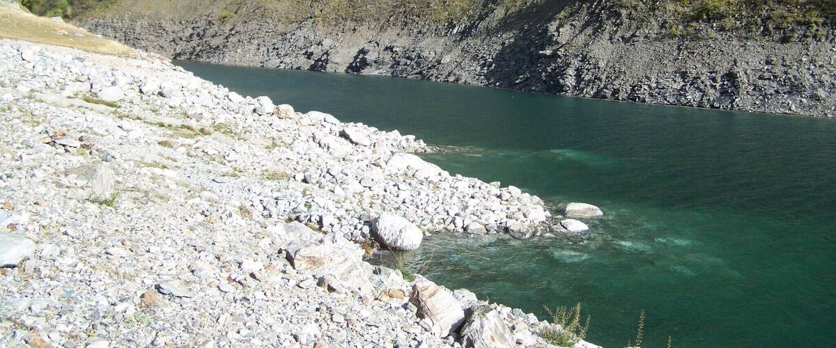 A rocky shoreline with clear water and a steep hillside in the background.