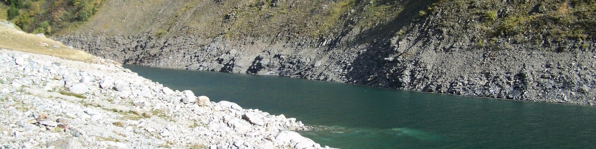 A rocky shoreline with clear water and a steep hillside in the background.