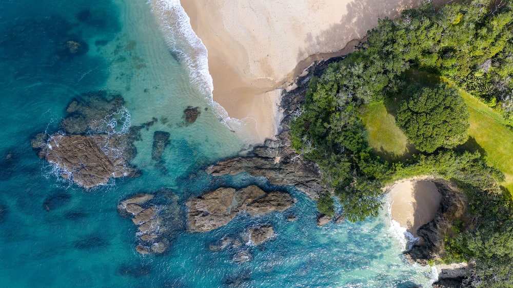 A coastal landscape with clear turquoise waters, a sandy beach, and a dense green forest area.