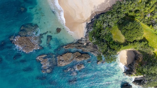 Aerial view of turquoise waters meeting the sandy shore near lush green headland, Langs Beach, Northland Region, New Zealand.