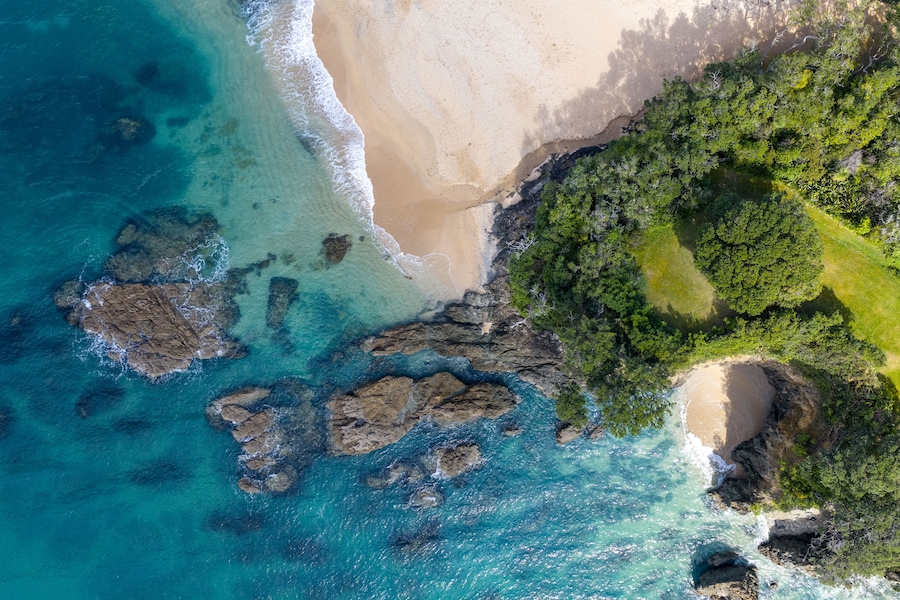 A coastal landscape with clear turquoise waters, a sandy beach, and a dense green forest area.