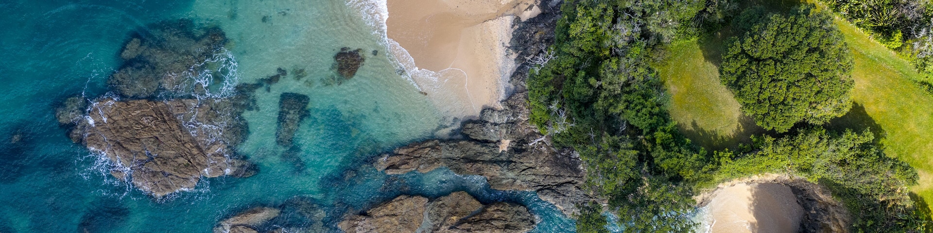 A coastal landscape with clear turquoise waters, a sandy beach, and a dense green forest area.