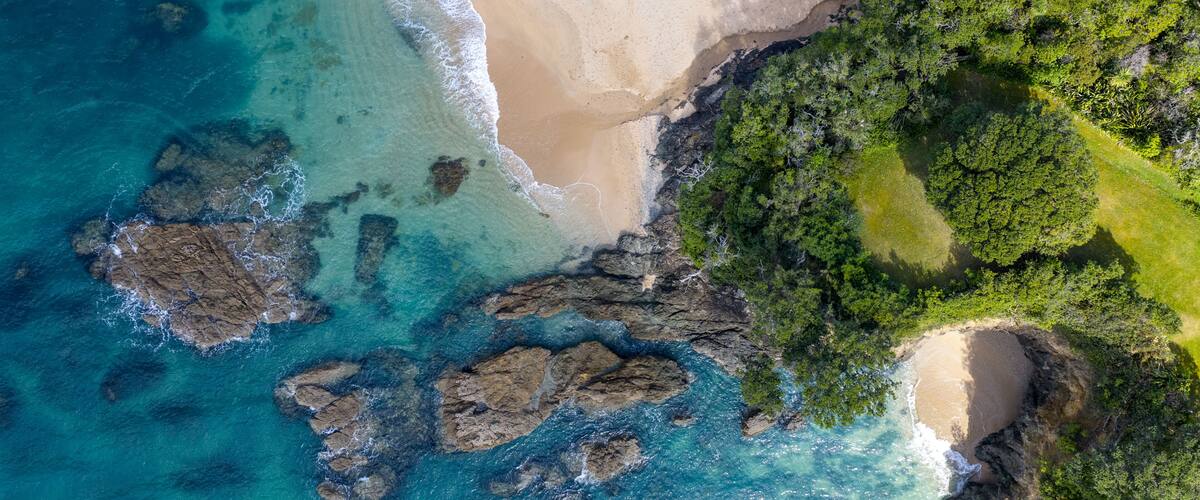 A coastal landscape with clear turquoise waters, a sandy beach, and a dense green forest area.