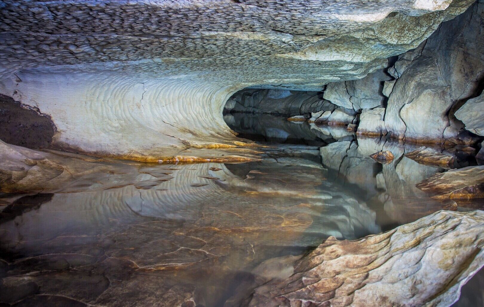 A cave with a reflective water surface and a rocky interior.