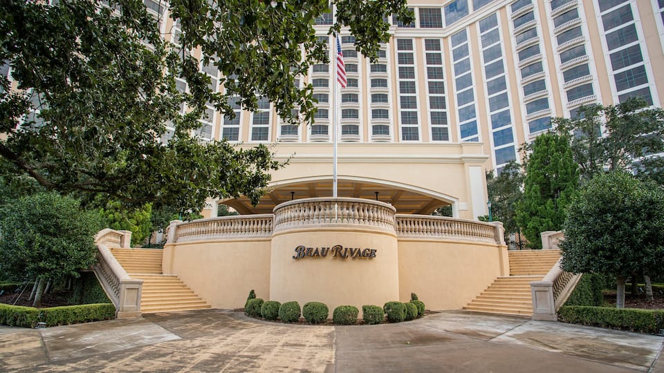 A grand entrance with a beige facade, a central archway, and a flag.