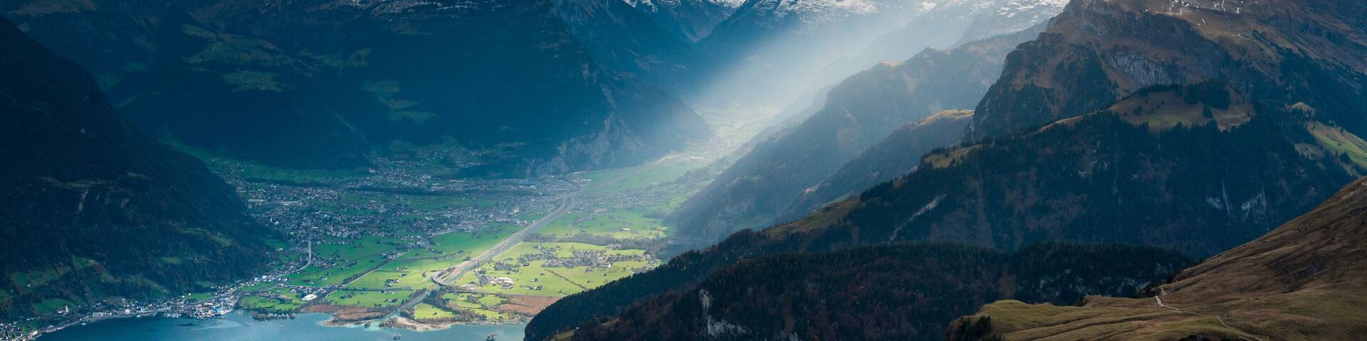 A mountainous landscape with snow-capped peaks, a valley with a river, and a town below.