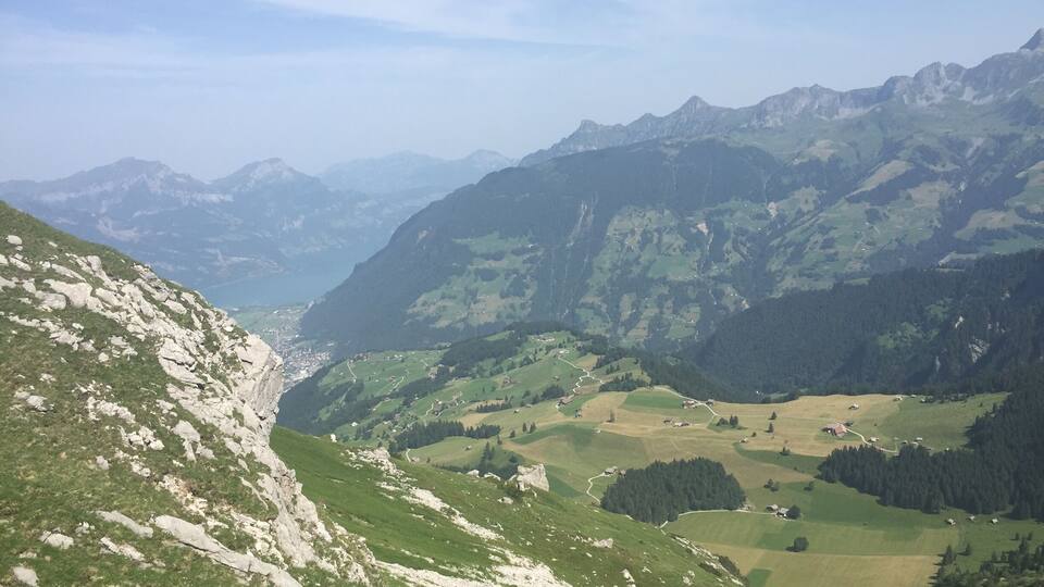 A mountainous landscape with a valley, winding roads, and scattered buildings.