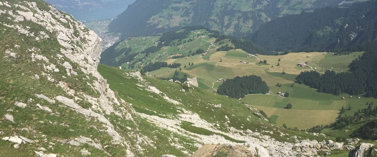 A mountainous landscape with a valley, winding roads, and scattered buildings.