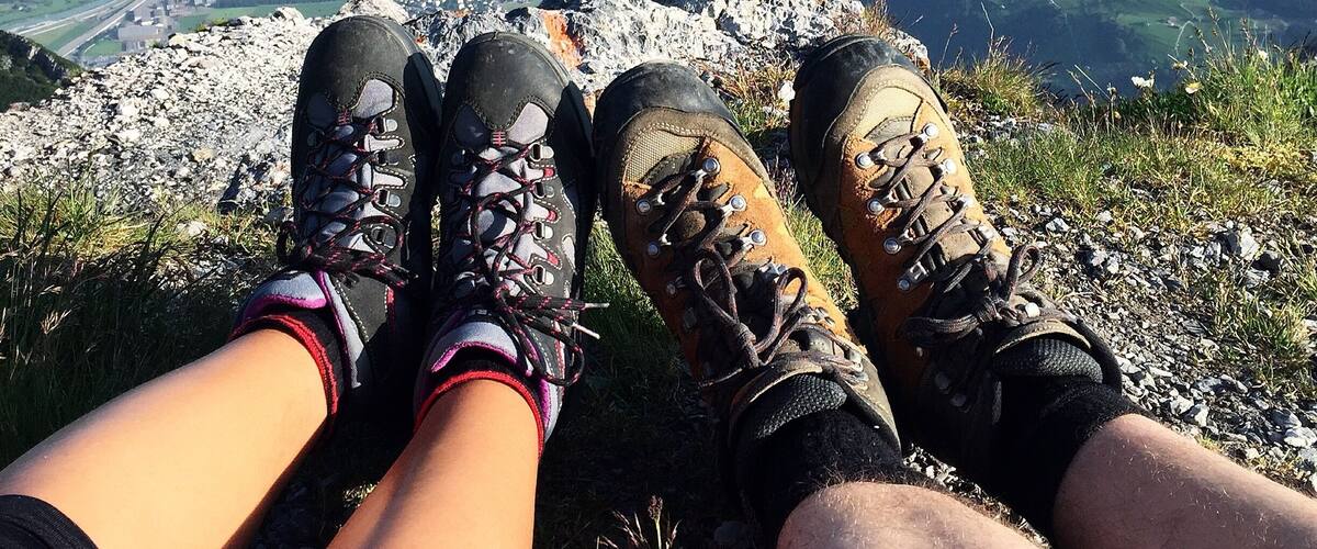 Une personne assise sur une montagne, portant des chaussures de randonnée, et d’où l’on peut admirer une vallée et un lac.