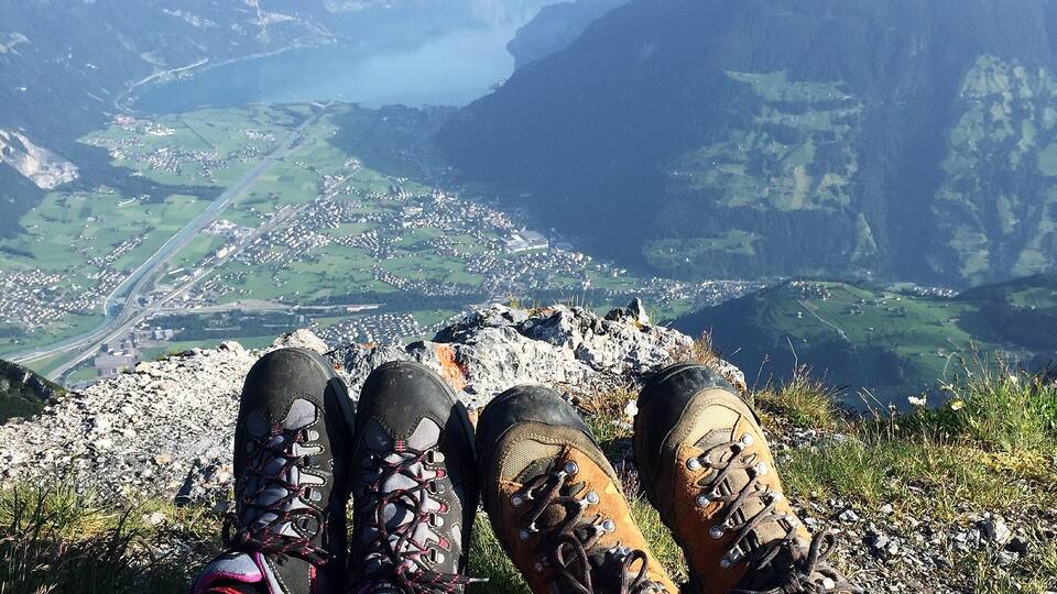 A person sitting on a mountain with hiking boots, overlooking a valley and a lake.