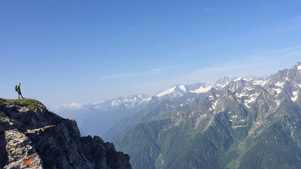 A hiker on a mountain peak with snow-capped mountains in the background.