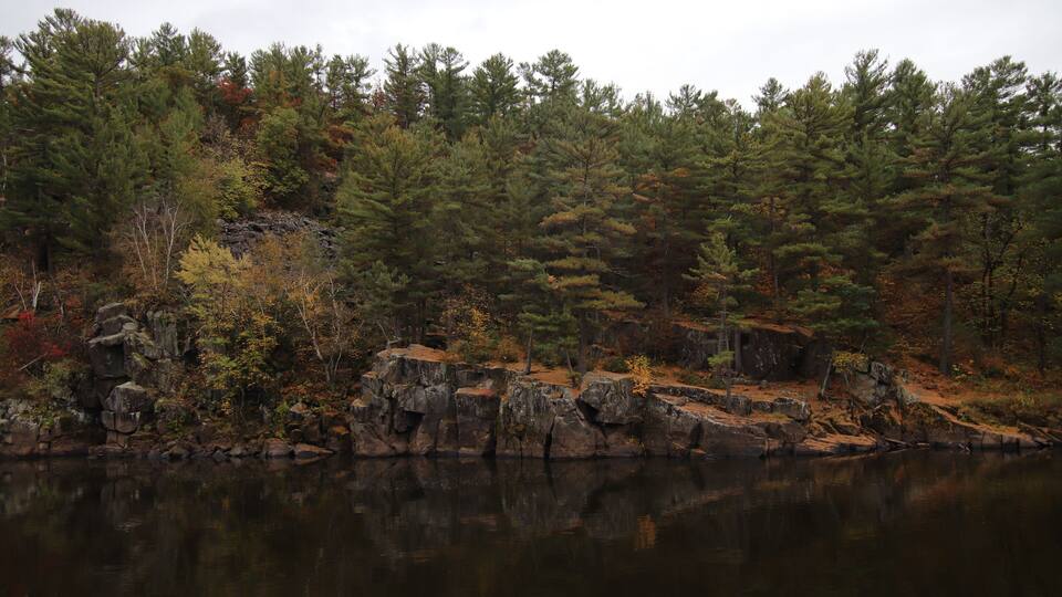 A calm lake surrounded by dense forest with autumn-colored trees and rocky outcrops.