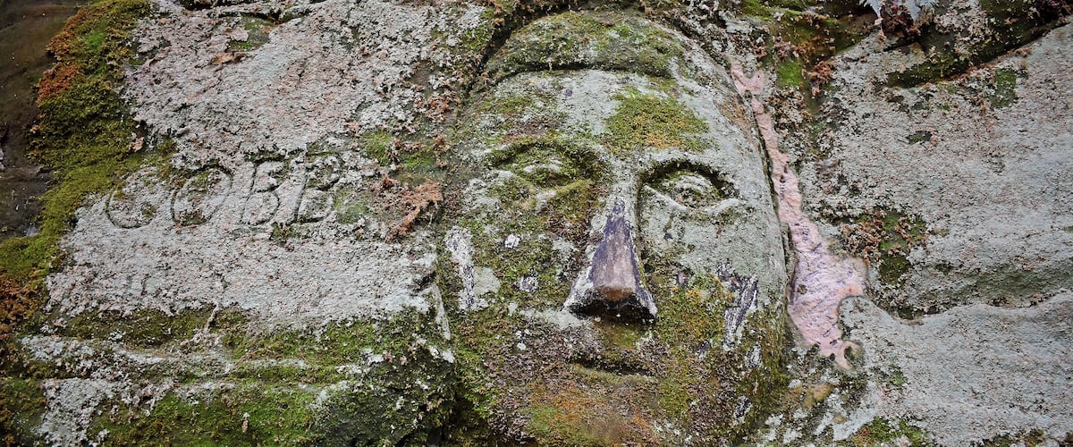 A moss-covered rock with a carved face.