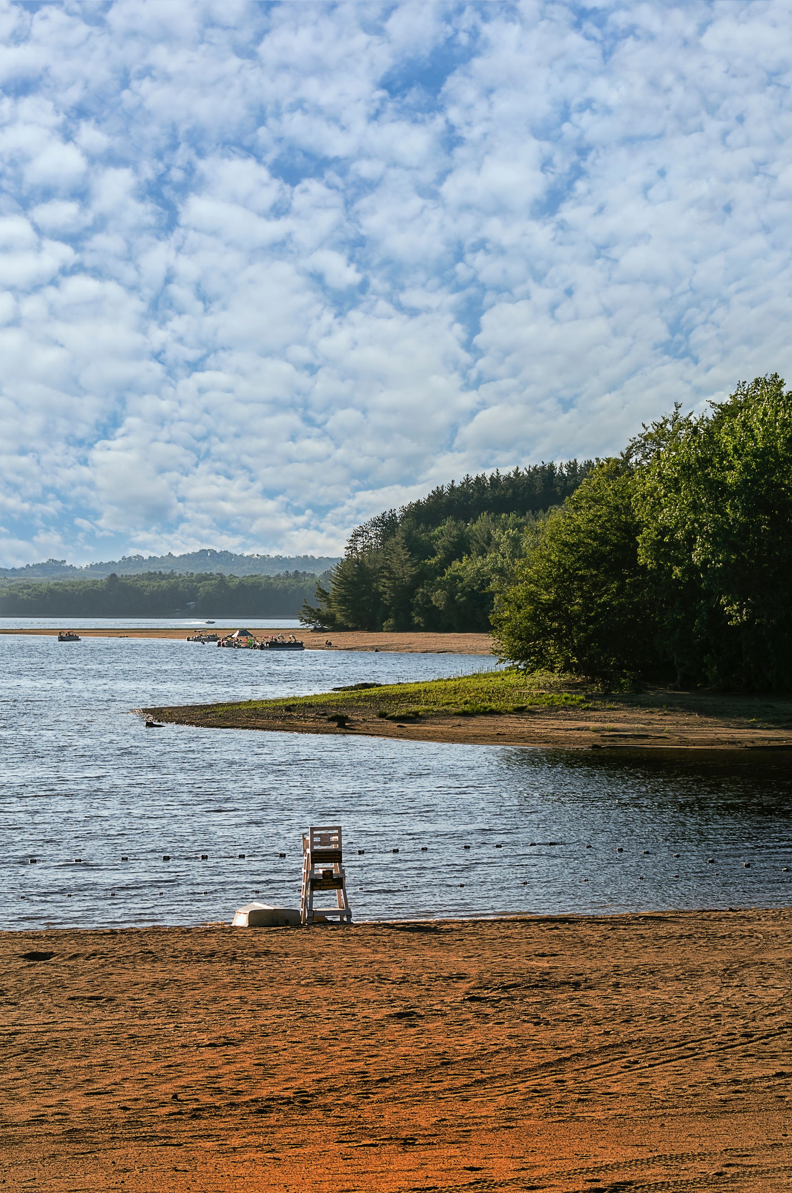 A beach with a lifeguard chair, calm water, and a forested hill in the background.