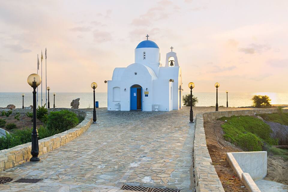 A white church with a blue dome and bell tower by the sea.