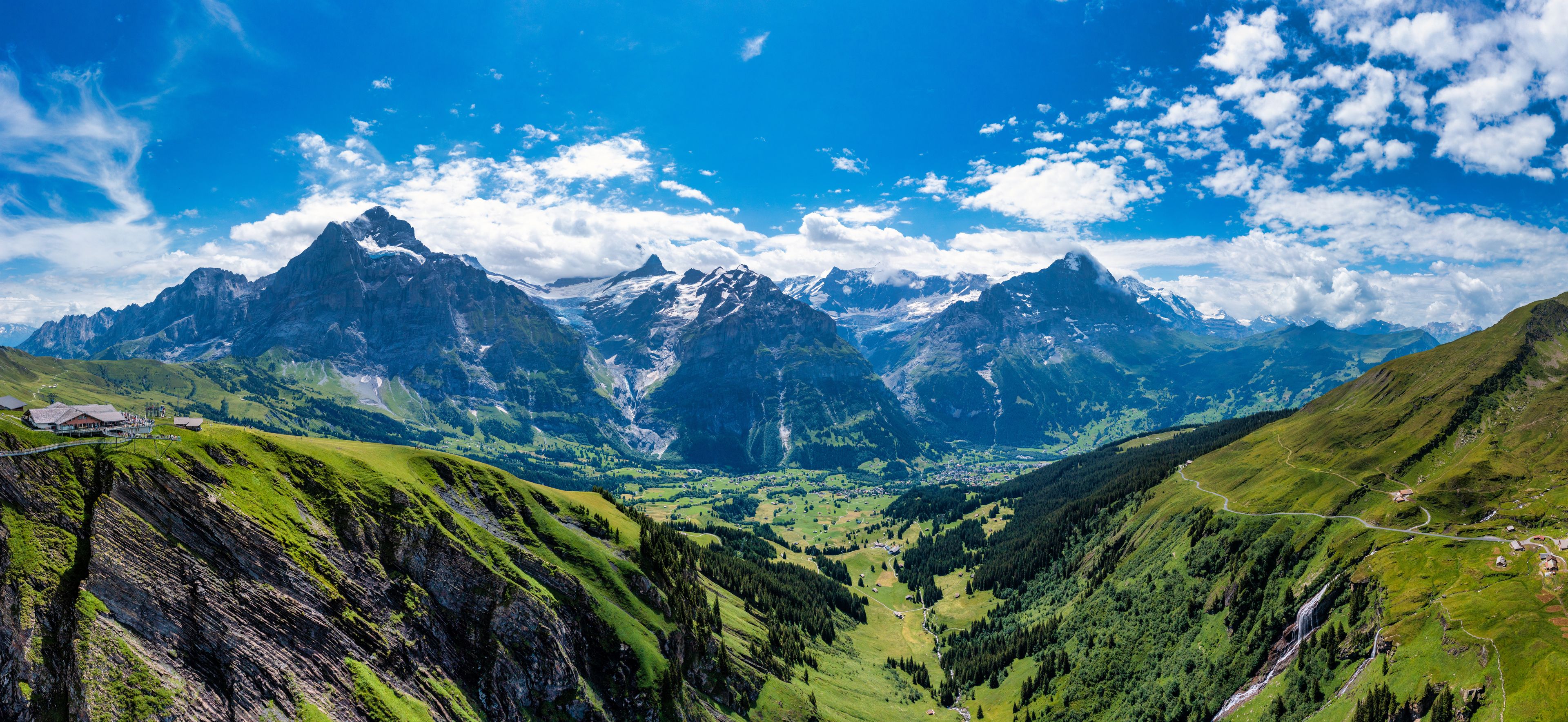 Un paysage montagneux avec une vallée, une route sinueuse et un petit bâtiment.