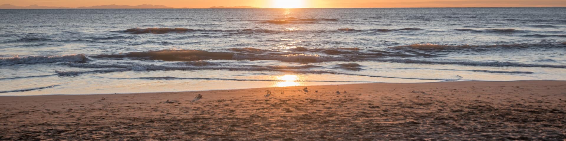 A beach at sunset with waves and a clear sky.