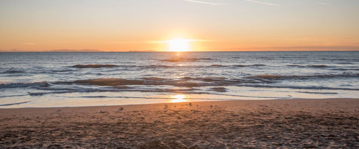 A beach at sunset with waves and a clear sky.
