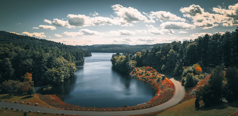 Un lago rodeado de colinas boscosas, una carretera sinuosa y un cielo despejado con nubes.