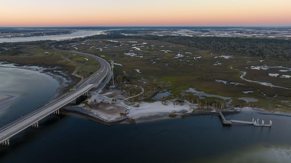 A coastal highway bridge over a marshy area with a sunset in the background.