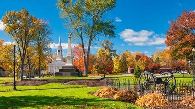 A park with a monument, a church, autumn trees, and a historical cannon.