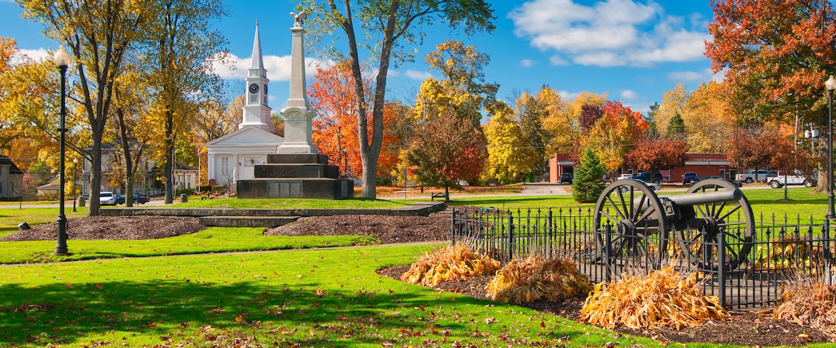 A park with a monument, a church, autumn trees, and a historical cannon.