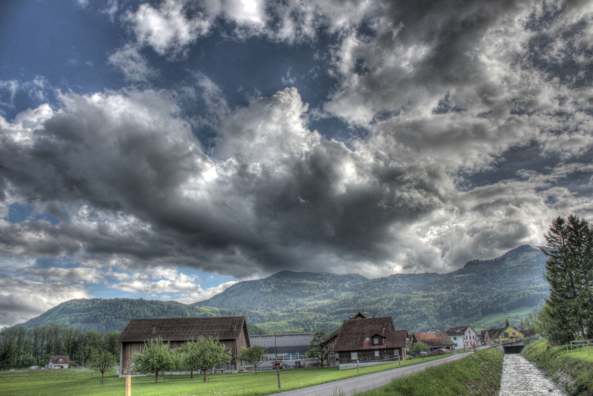 A rural landscape with a mountain range, a river, and several houses.