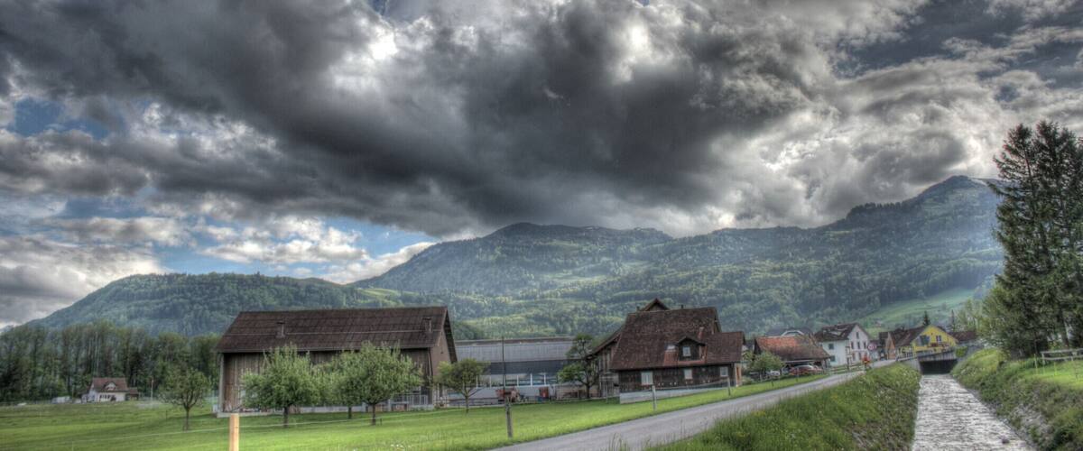 A rural landscape with a mountain range, a river, and several houses.