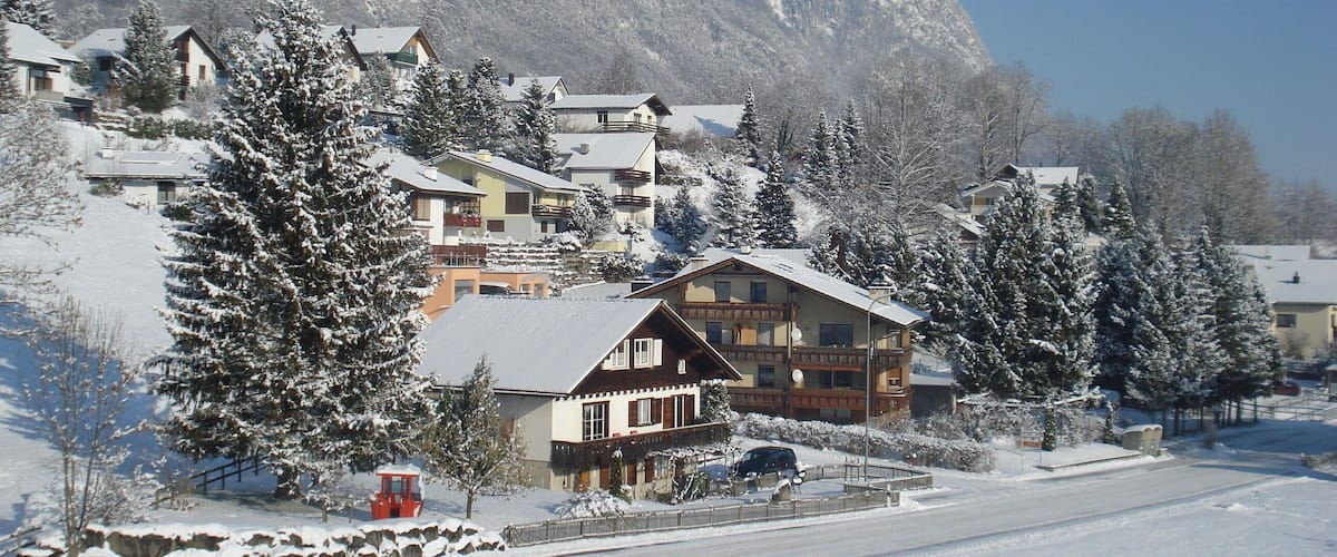 A snow-covered village with houses, a red train, and mountains in the background.