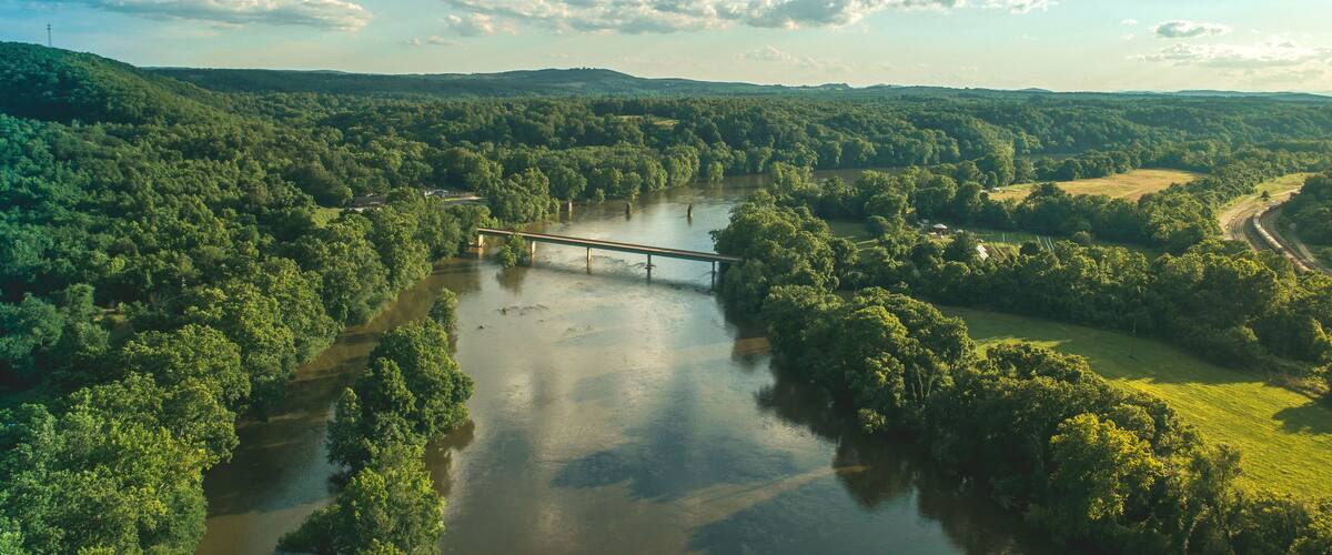 A river with a bridge, surrounded by dense forest and hills.