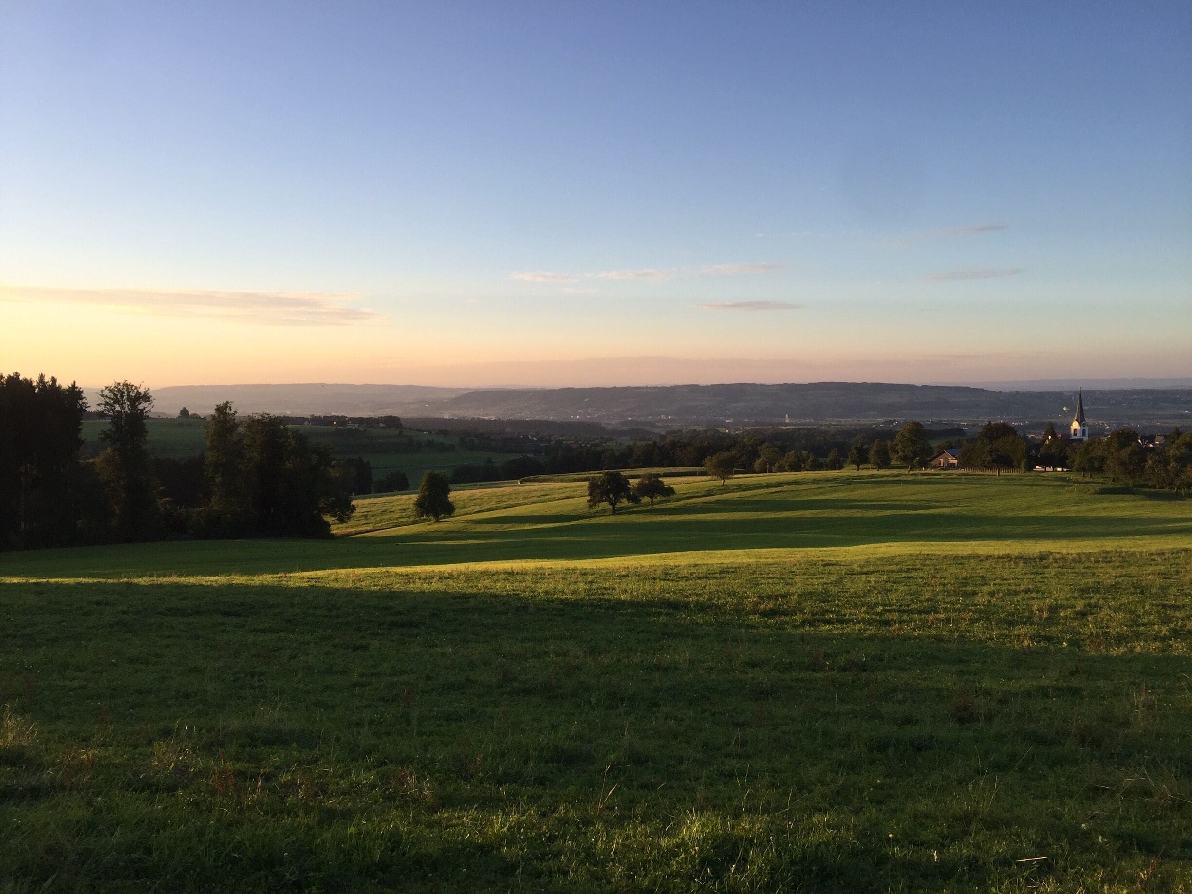 A grassy field with a church in the distance.