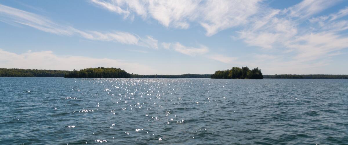 A calm lake with a small island in the distance and a clear blue sky with wispy clouds.